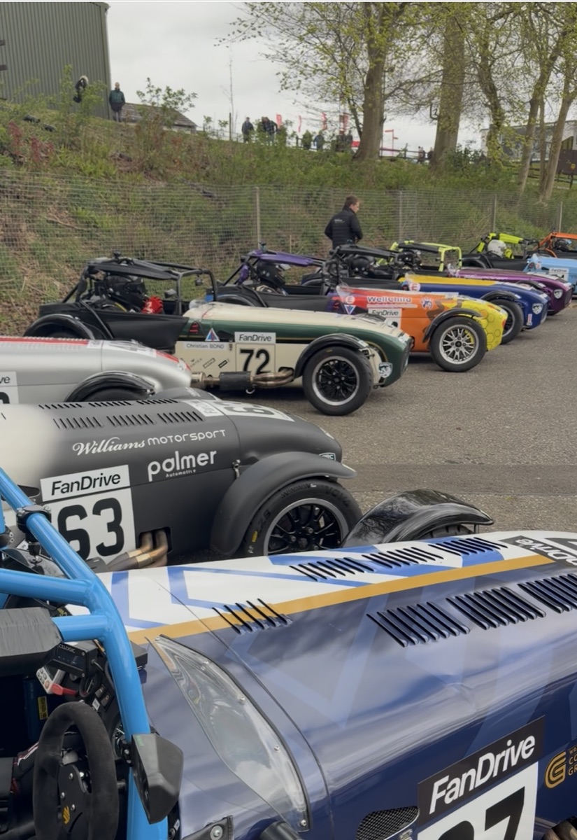 A line of Caterham race cars in the paddock, each carrying FanDrive branding alongside their race numbers