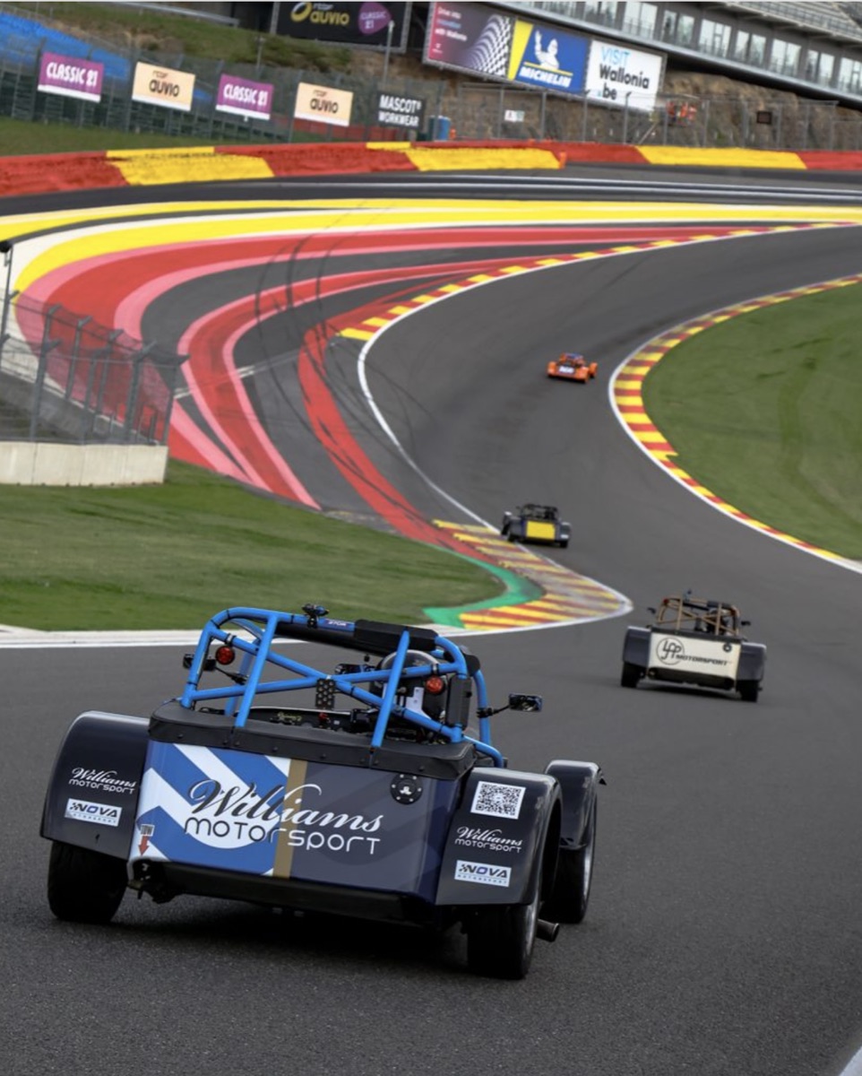 Caterham race cars climbing Eau Rouge at Spa-Francorchamps, the nearest carrying a QR code on its rear panel