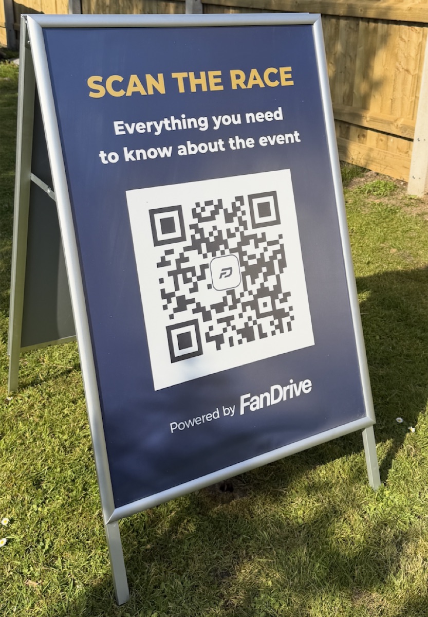 A trackside A-board reading 'Scan the race — everything you need to know about the event', with a large QR code, powered by FanDrive